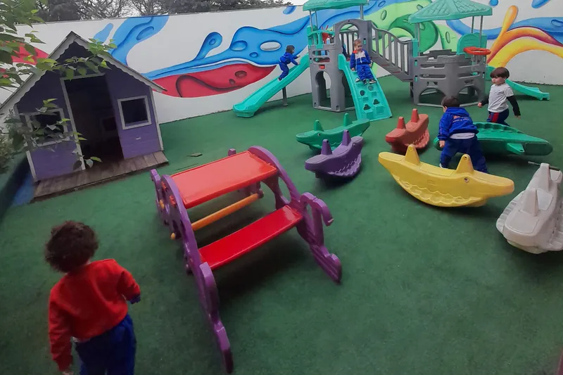 Crianças brincando no pátio da Escola Magia, entre a casinha, o brinquedo grande e os balanços