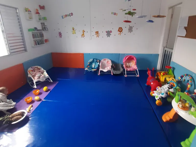 A sala do berçário, com o tatame azul, as cadeirinhas de bebê e os brinquedos junto à parede